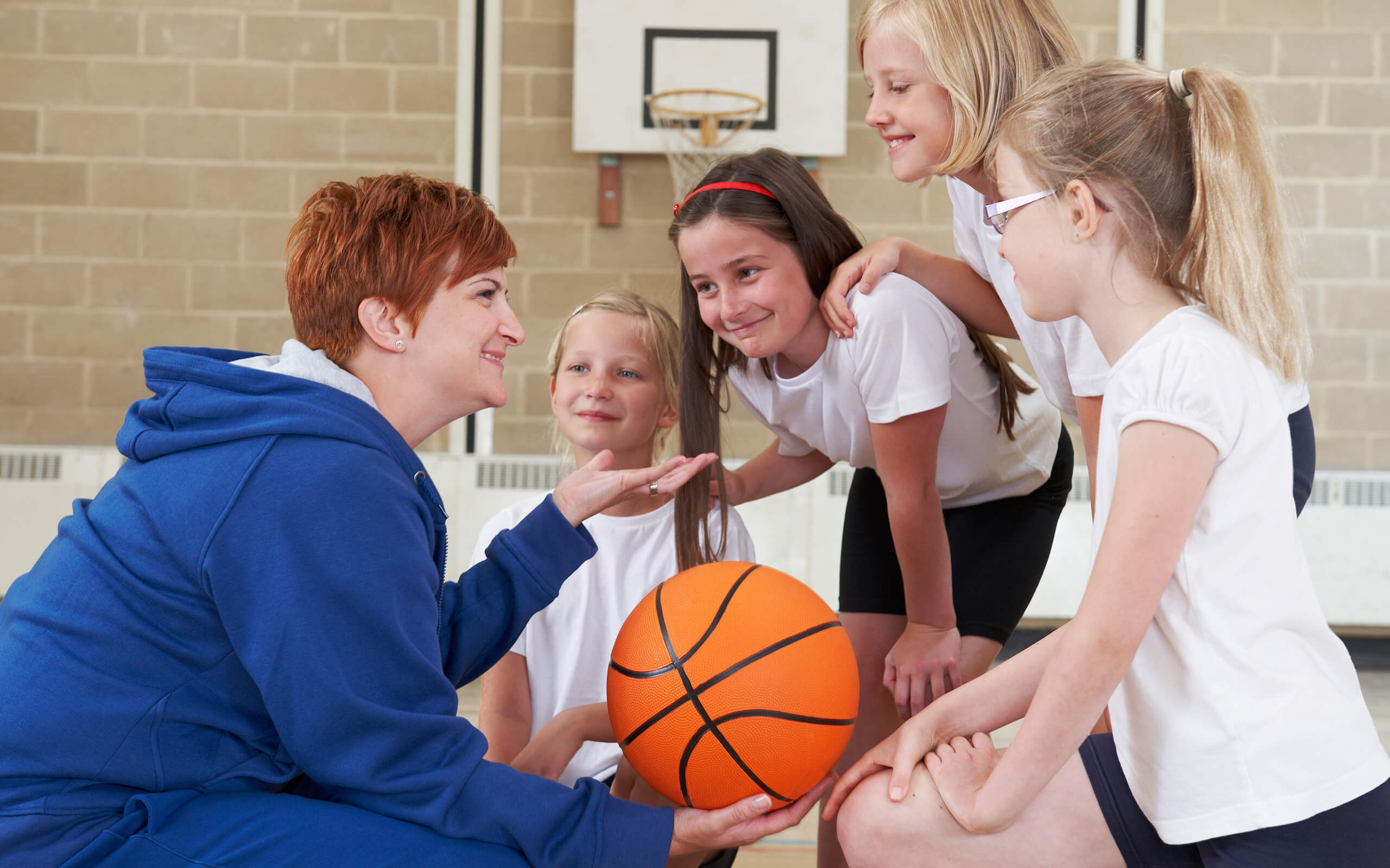 Primary Physical Education | female holding basketball speaking to children 
