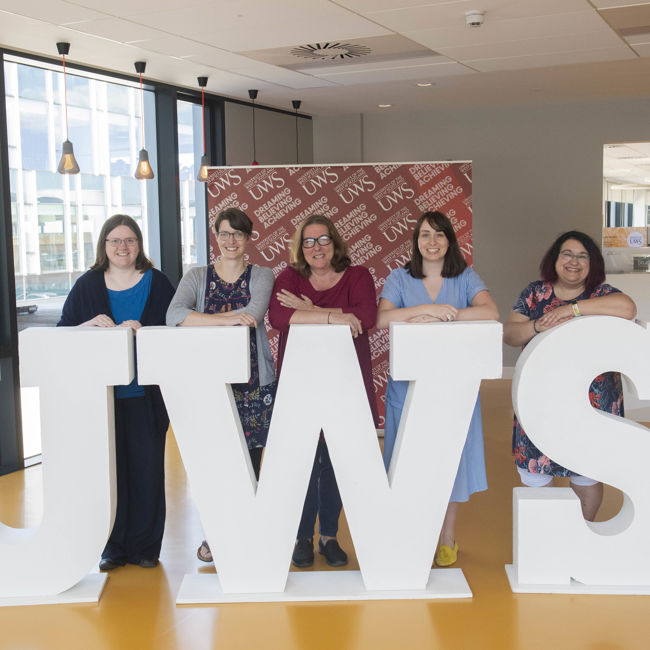 Image shows five colleagues standing behind four-foot tall white letters spelling UWS, for University of the West of Scotland. The colleagues are all members of UWS Academy, the institution's academic development unit. From left: Dr Lindsay Coyle, Dr Stephanie Zihms, Dr Jane MacKenzie (head of UWS Academy), Dr Eilidh Kane and Claire Mackie.