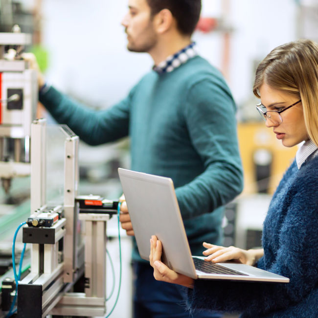 Students with laptop operating machinery in lab
