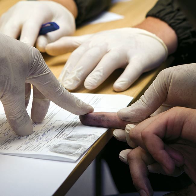 Gloved hand taking fingerprints of another hand