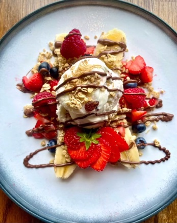 Banana split ice-cream presented on a late, with bananas, blueberries, raspberries, strawberries and chocolate sauce
